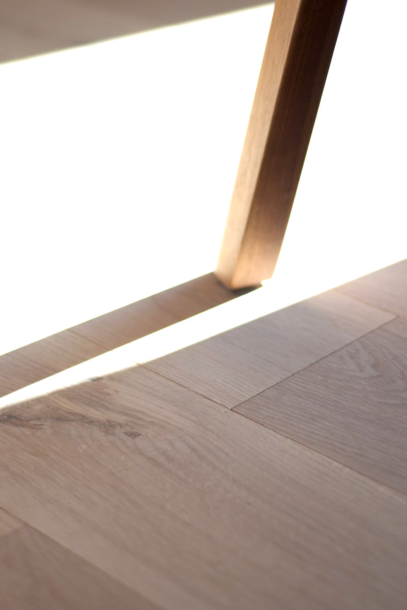 Sun shining on a chair leg on Scandinavian white oak flooring Astrid by Stuga. A knot and medullary rays shine through on the wood surface
