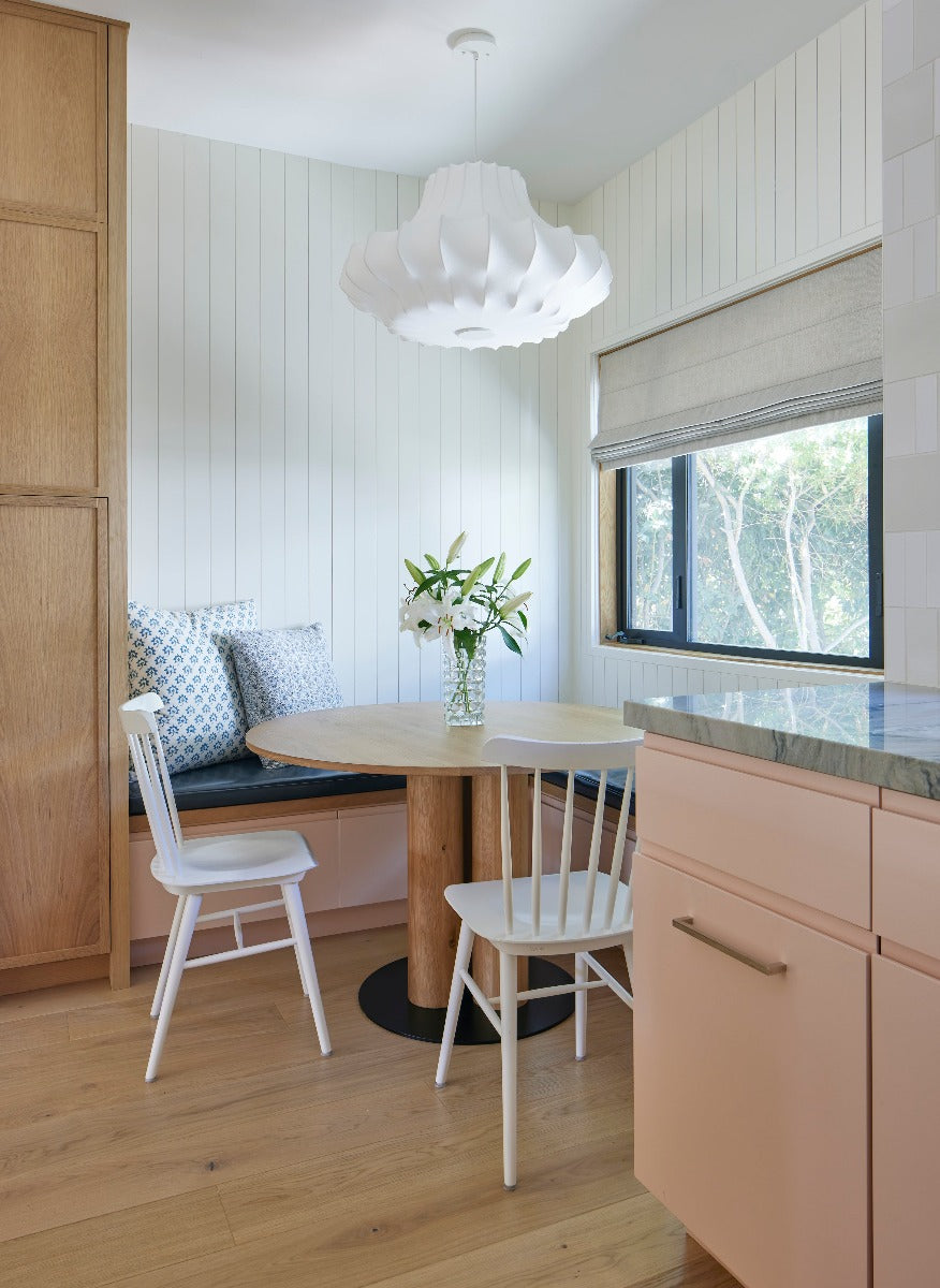 Wide plank blonde Scandinavian flooring in a breakfast nook with pink cabinets