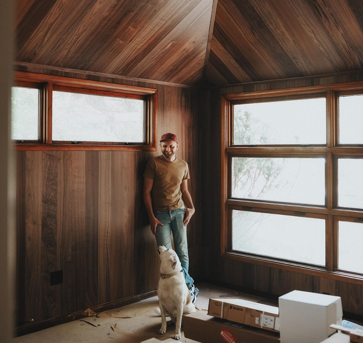 Man and dog in a cabin living room with walnut flooring on the walls and ceiling