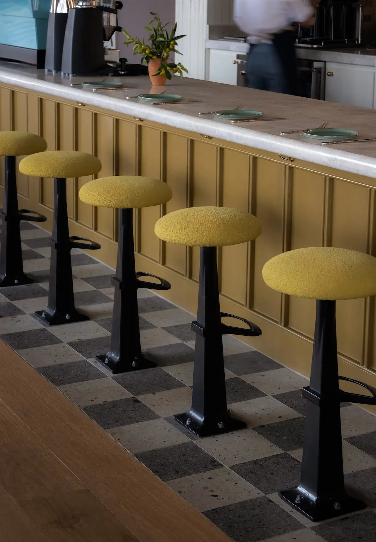 Yellow bar stools in front of a counter with warm hardwood flooring and checkered tile