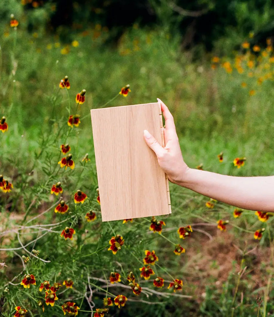 A sample of Scandinavian wood flooring held by a hand in a field of flowers