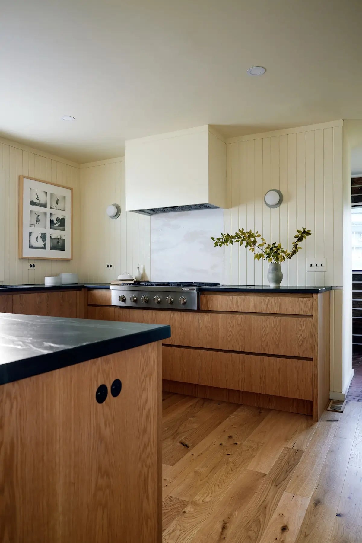 Modern kitchen with rustic wood floors by Stuga, wooden cabinets, black soapstone countertops, and a central island.