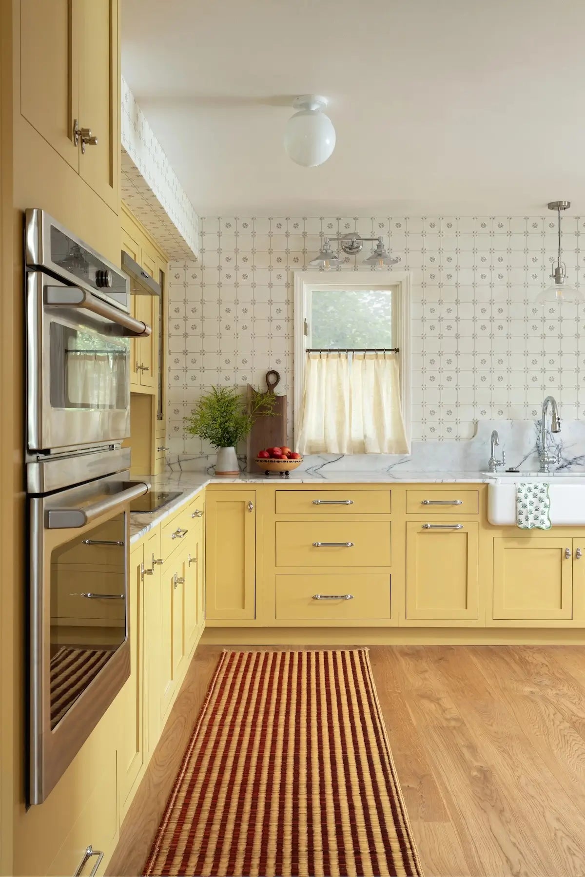 Modern kitchen with yellow cabinets, stainless steel appliances, and a wooden floor.