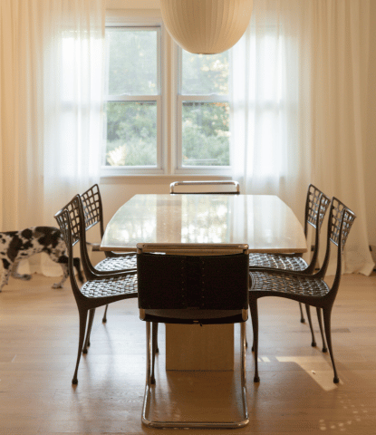 Midcentury dining room with travertine table, black chairs, and white oak flooring. A great dane puppy walks in the background