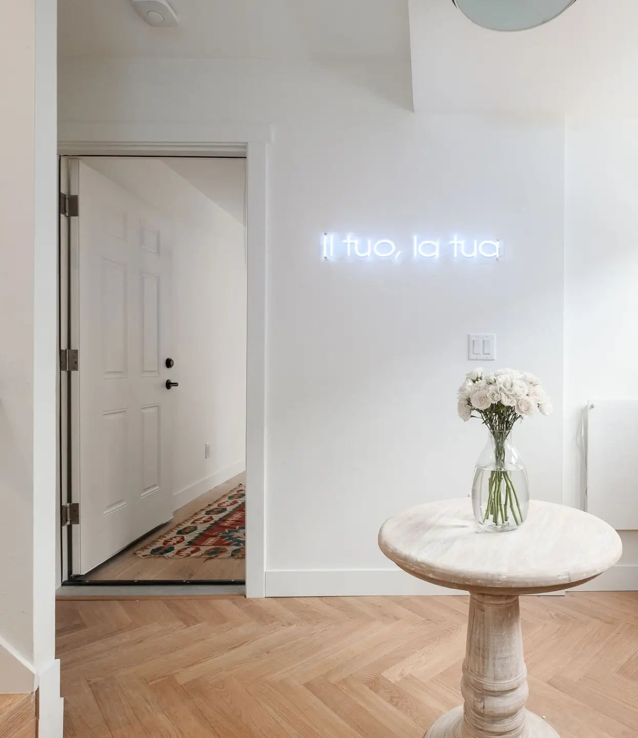 Herringbone wood flooring by Stuga in a foyer with marble table and neon wall art